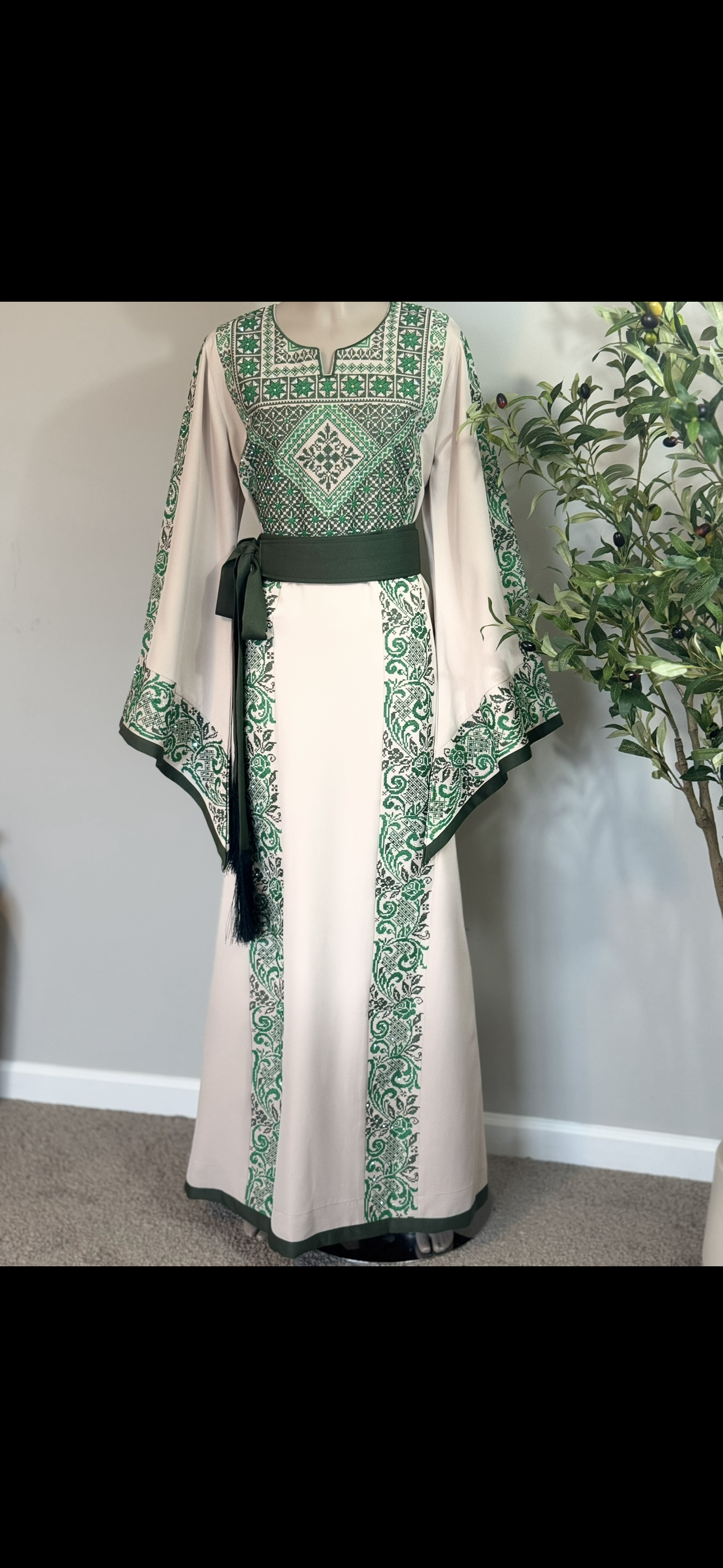 Beige fabric thobe with green embroidery with matching satin belt .