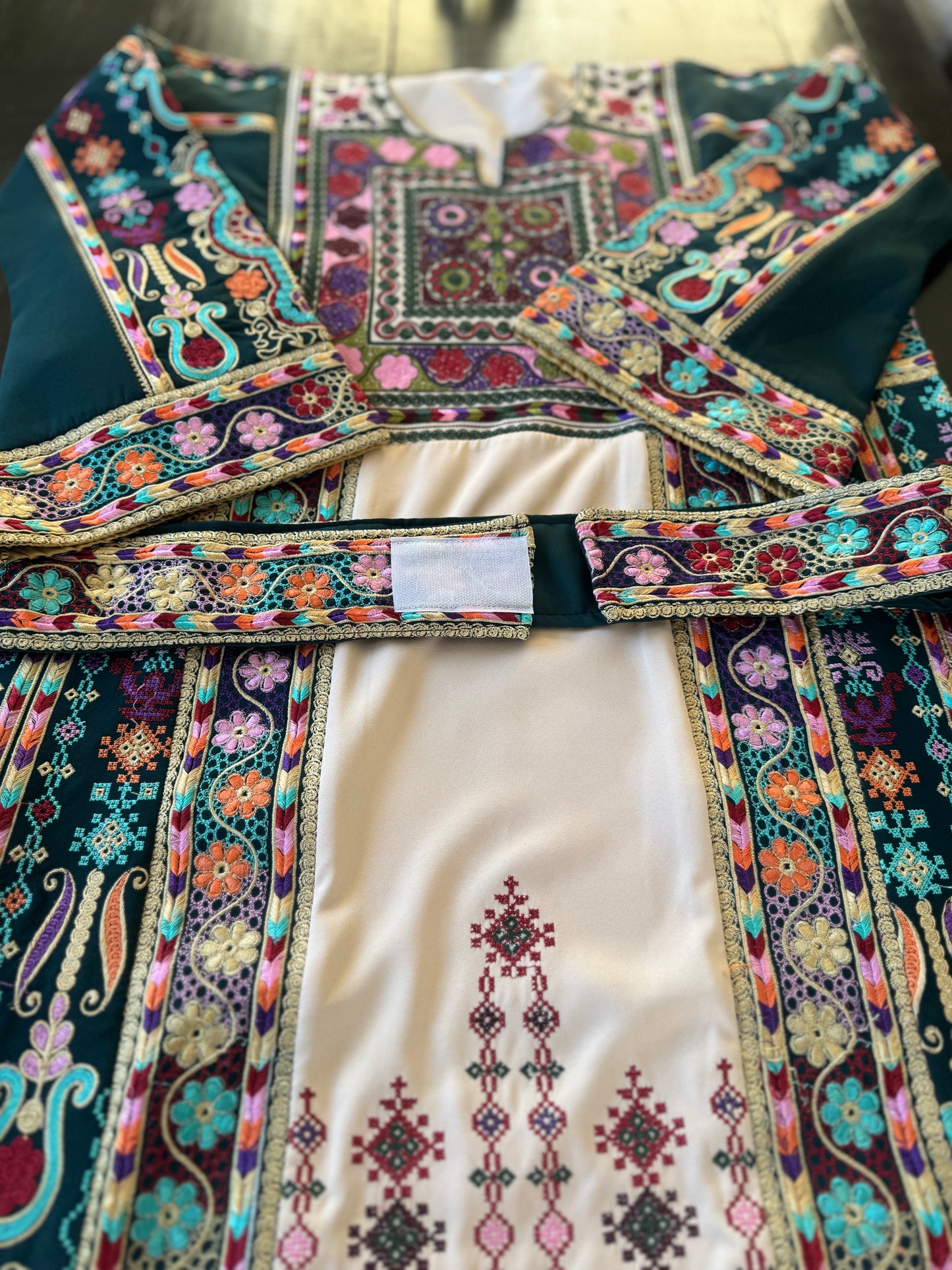 Light beige thobe with green fabric and colorful embroidery.